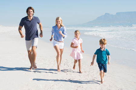 Family running on the beach. Happy beautiful family running and looking at camera. Happy family having fun walking on the beach.の写真素材