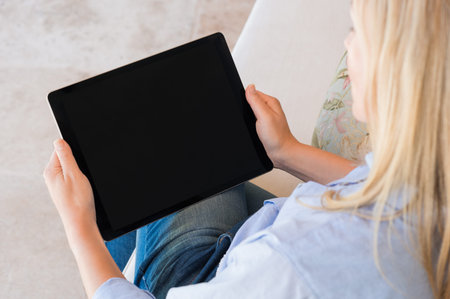 High view of woman working on digital tablet with black screen. Mature woman sitting on couch and...