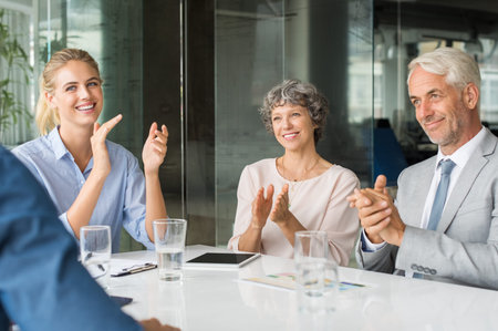 Group of business people meeting in corporate conference room, applauding at a coworker during his...