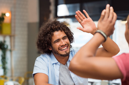 Portrait of friends giving high five at cafe while having lunch. Young guys friends giving a high five, slapping each others hand in congratulations while sitting in cafeteria.の写真素材