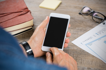 Close up of a man using mobile phone on wooden desk. Businessman hand holding a smartphone and typing on touchscreen. Casual businessman showing display of cellphone.の写真素材