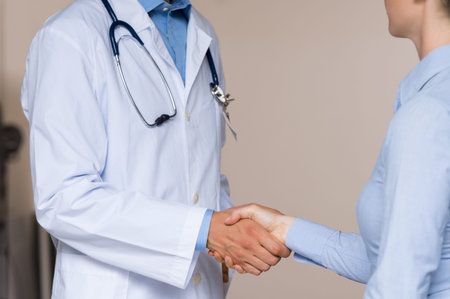 Doctor shakes hand with patient at hospital. Close up of healthcare professional shaking hands with new doctor joining. Doctor and woman patient handshake.の写真素材