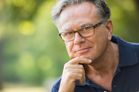 Close up face of satisfied senior man at park looking at camera. Portrait of mature man sitting in...