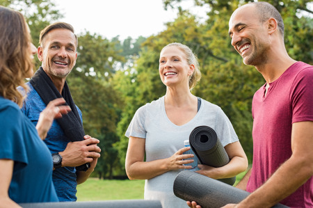 Happy multiethnic group of mature people holding yoga mat and towel in conversation after exercising at park. Happy senior men and smiling women talking to each other after an exercising class outdoor.の写真素材