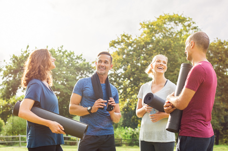 Group of multiethnic people talking to each other after exercising at park. Couples in a conversation after enjoying yoga session outdoor. Cheerful group of mature friends relaxing after yoga.の写真素材
