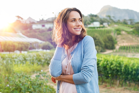 Portrait of mature brunette woman relaxing at park and looking away. Happy woman relaxing outdoor at sunset. Smiling mature woman thinking.の写真素材