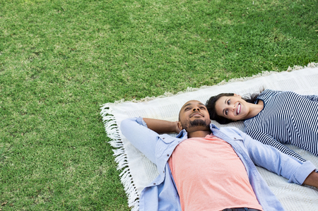 Young multiethnic couple lying on blanket on grass. Latin woman with her african boyfriend relaxing on picnic blanket outdoor. Mature happy couple in love lying on grass with copy space.の写真素材
