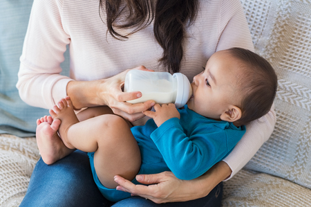 Little infant baby lying on mothers hand drinking milk from bottle. Newborn baby drinking milk from bottle. Cute toddler with milk bottle on leg of mother.の写真素材