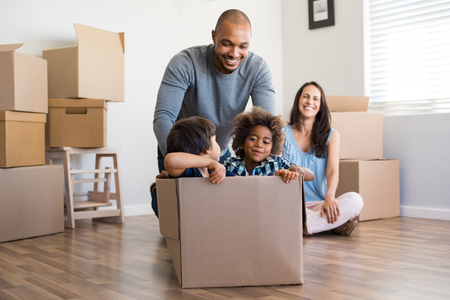 Happy african american father playing with children sitting in carton box at new home. Happy multiethinc family enjoying new home. Young parents and sons having fun during moving house.の写真素材
