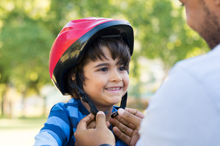 Father helping cheerful son wearing helmet for cycle. Excited little boy getting ready by wearing bike helmet to start cycling. Happy cute boy learn to ride a bike with his dad.の写真素材
