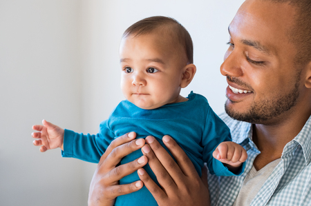 Portrait of loving young man holding baby at home. Close up of happy black father with his little boy smiling. Young african father embracing his cute toddler.の写真素材