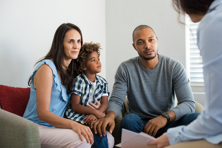 Serious couple with son in a deep conversation with family counselor. Multiethnic parents talking about adoption with their counselor. Family at the financial planning consultation.の写真素材