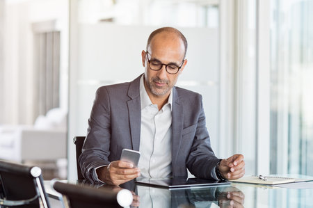 Mature business man in formal clothing wearing spectacles using mobile phone. Serious businessman...
