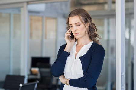 Serious business woman looking worried while talking on the phone in conference room. Frustrated businesswoman in office using mobile phone. Unhappy mature woman talking on phone call on smartphone.の写真素材