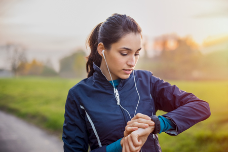 Young athlete listening to music during workout at park and adjusting smart watch.