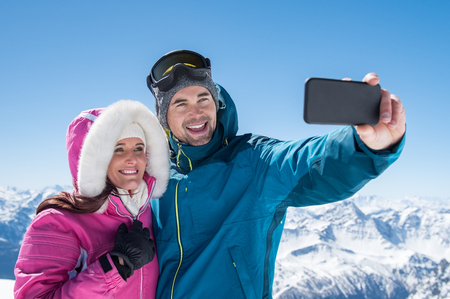Man taking selfie with cheerful girlfriend over snowy mountains.の写真素材
