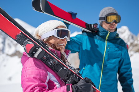 Smiling young couple with ski on shoulder standing on mountain covered by snow.の写真素材