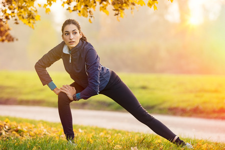 Young woman stretching and warming up at park during sunset.の写真素材