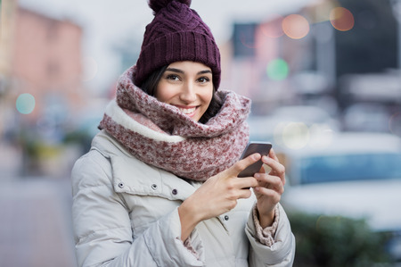 Happy young woman holding smartphone and looking at camera.の写真素材