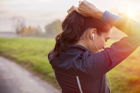 Woman tying hair in ponytail getting ready for exercising at sunset.の写真素材