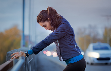 Athletic woman resting after jogging and leaning on a parapet of the bridge.の写真素材