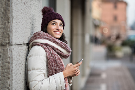 Pensive young woman holding smartphone and looking up.の写真素材