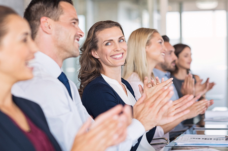 Businessmen and business women sitting in a row and applauding at meeting. Successful businesspeople clapping hands after presentation. Happy group of business people sitting in a row at conference.の写真素材