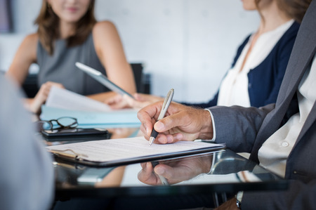 Closeup of hand of businessman holding pen and analyzing report during board meeting. Business people writing on document during annual meeting. Detail hand of business man fill the business contract.の写真素材