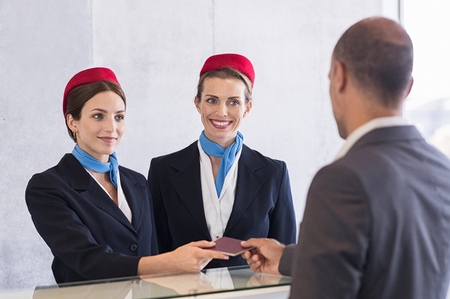 Woman in checkin counter taking passport for verification from passenger man. Happy smiling hostess at check in working with her colleague. Businessman on a business trip in airport.の写真素材