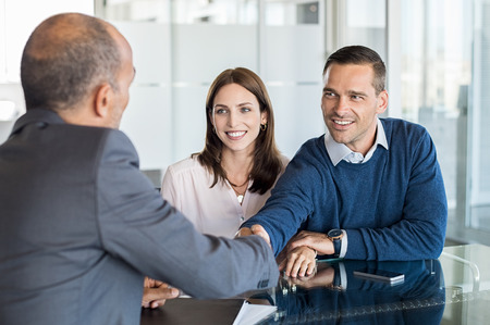 Businessman shaking hand with a young couple in office. Bank agent and his client shaking hands in conference room. Happy smiling couple seal a deal with their personal financial advisor.の写真素材