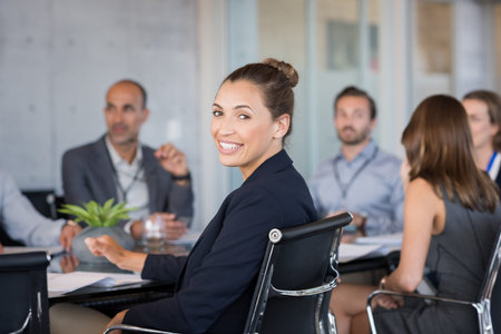 Young beautiful businesswoman with colleagues sitting in a modern board room. Proud smiling business...