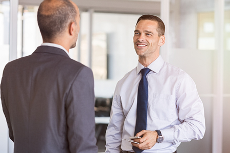 Two businessmen having happy conversation in office. Employee talking to boss discussing about new project. Mid adult businessman meeting senior manager in a modern office.の写真素材