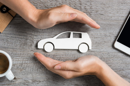 Hands protecting icon of car over wooden table. Top view of hands showing gesture of protecting car....