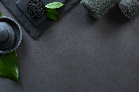 Top view of two gray rolled towels with hot stones pile with copy space. High angle view of male beauty treatment set with green leaf and black salt. Luxury and elegant spa setting on black background.の写真素材