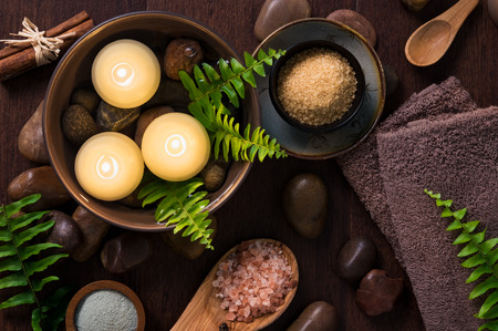 Beautiful spa composition on wooden background with floating candles in a water bowl. Burning candles with himalayan salt and spa products on brown background. Luxury spa set with towels and fern leaves.の写真素材