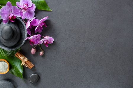 Top view of hot stones setting for massage treatment on blackboard with copy space. High angle view of beautiful orchids on green leaf with black stones pile for spa therapy. Elegant and luxury spa concept on gray background.の写真素材