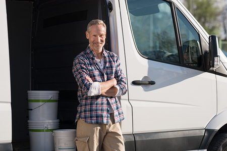 Portrait of painter standing next to his van with paint container. Decorator standing next to van and looking at camera. Happy smiling worker leaning on his white truck with folded arms.の写真素材