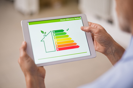 Hand holding digital tablet and looking at house efficiency rating. Detail of house efficiency rating on digital tablet screen. Concept of ecological and bio energetic house. Energy class.の写真素材