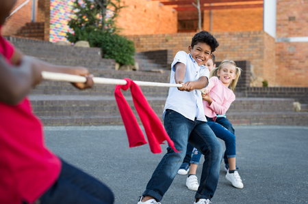 Happy group of kids playing tug of war outdoor. Young boys and girls as a team in tug-of-war outside the school. Group of happy multiethnic friends playing with rope in city park.の写真素材