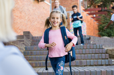 Happy cute girl running with stretched arms towards mother after school. Young school child feeling happy after lesson at primary school. Elementary student kids running into mother's hands to hug her after school.