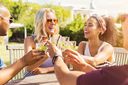 Two happy young couples toasting with glasses of cocktails. Young beautiful women and men drinking lemonade and smiling.の写真素材