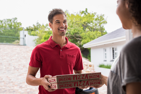 Smiling delivery boy in red t-shirt delivering two pizza boxes to woman. Happy young delivery man giving pizza to customer on the doorstep. Smiling woman receiving take away food from deliveryman.の写真素材
