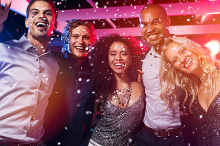 Happy young friends dancing at party night with confetti. Group of beautiful women and elegant men...