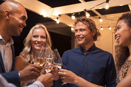 Group of multiethnic friends toasting champagne flutes at outside party night. Young men and smiling women enjoying outdoor evening party.の写真素材