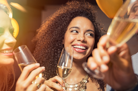 Happy young african woman holding wine glass with friends at party. Portrait of beautiful black girl enjoying new yearâs eve with friends.の写真素材