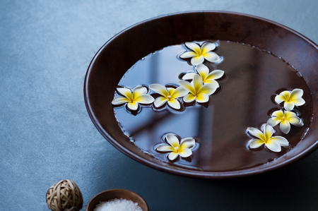 Closeup of frangipani flowers floating in bowl of water at wellness center. White flowers in wooden bowl with water for aroma therapy at spa. Spa setting for beauty treatment.の写真素材