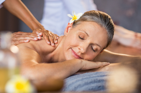 Woman lying on a spa bed and getting a relaxing massage. Serene mature woman having oil massage on her back. Portrait of senior woman with closed eyes having spa treatment.の写真素材