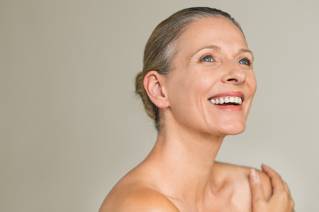 Portrait of a cheerful senior woman smiling while looking away isolated on gray background. Happy mature woman after spa massage and anti-aging treatment on face.の写真素材