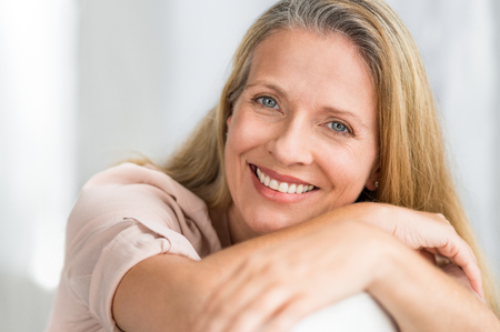 Portrait of happy senior woman relaxing on sofa. Closeup face of mature blonde woman smiling and looking at camera. Retired lady in casual leaning on couch.の写真素材