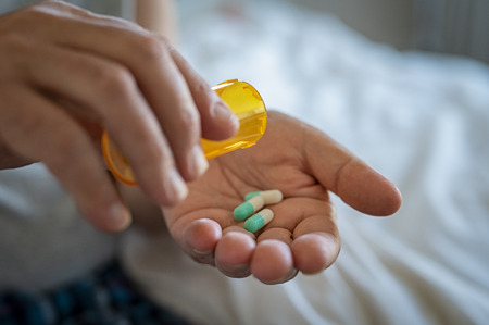 Closeup of man hand pouring capsules from a pill bottle into hand. Senior man taking daily medicine to consume. Close up of male hands taking daily dose of drug.の写真素材